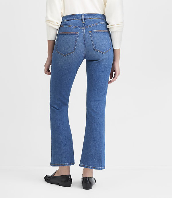 A person wearing flared jeans and black loafers stands against a plain white background.
