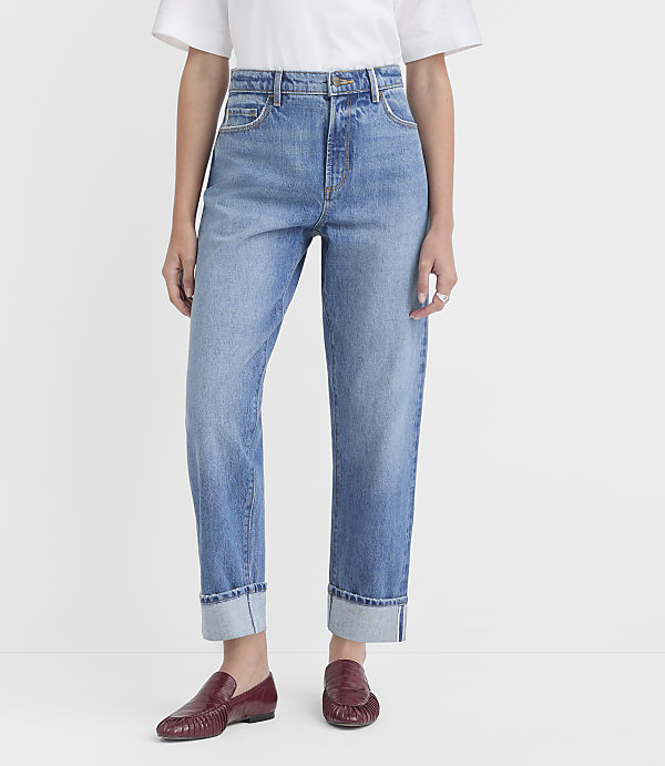 A person wearing cuffed light-wash jeans and burgundy loafers stands against a plain white background.