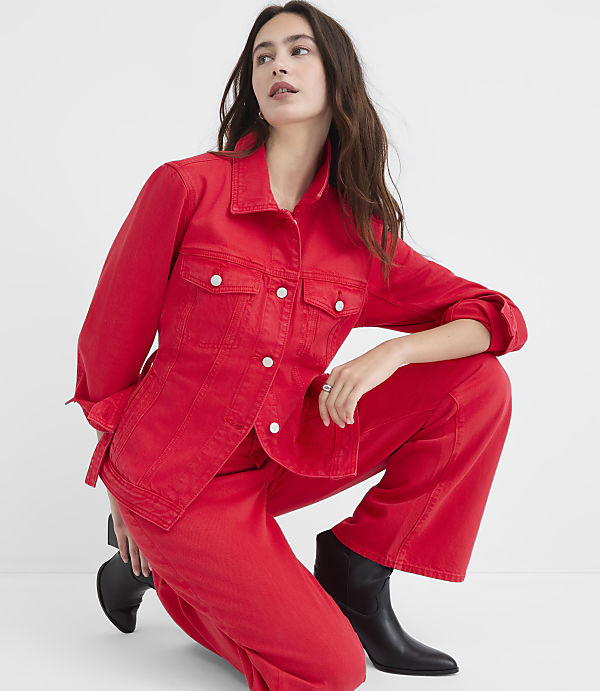 A woman in a red denim jacket and pants crouches in the foreground against a plain white background.