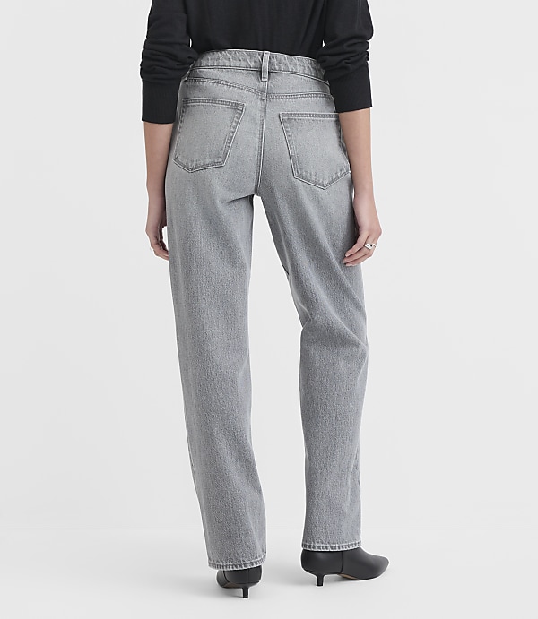 A person wearing grey jeans and black shoes stands against a plain white background.