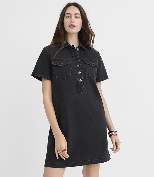 A woman in a dark denim shirt dress stands against a plain white background.
