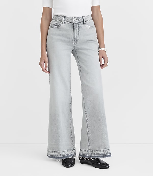 A person stands in light-wash flared jeans with frayed hems and black loafers against a plain white background.