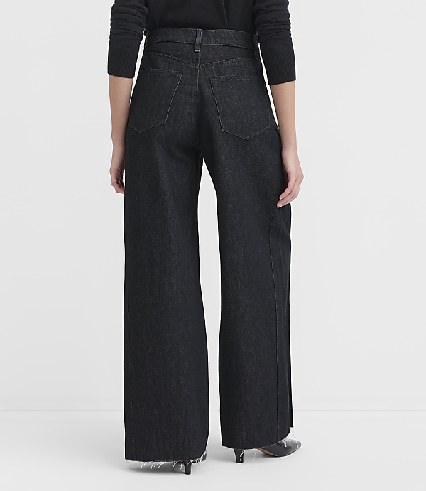 A person wearing dark wash wide-leg jeans stands against a plain white background.