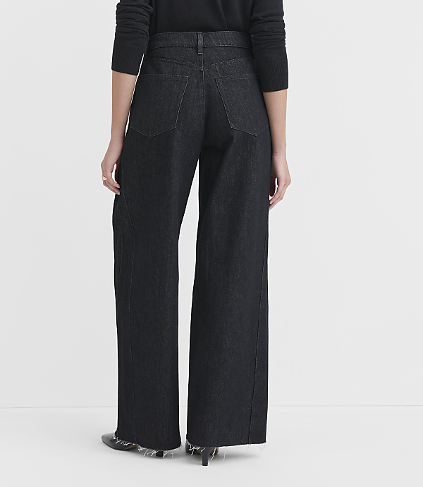 A person wearing dark wide-leg jeans and a black top stands against a plain white background.