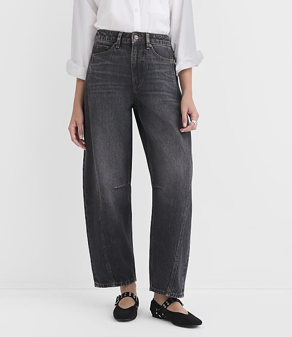 A person wearing dark wash, wide-leg jeans and black studded flats stands against a plain white background.