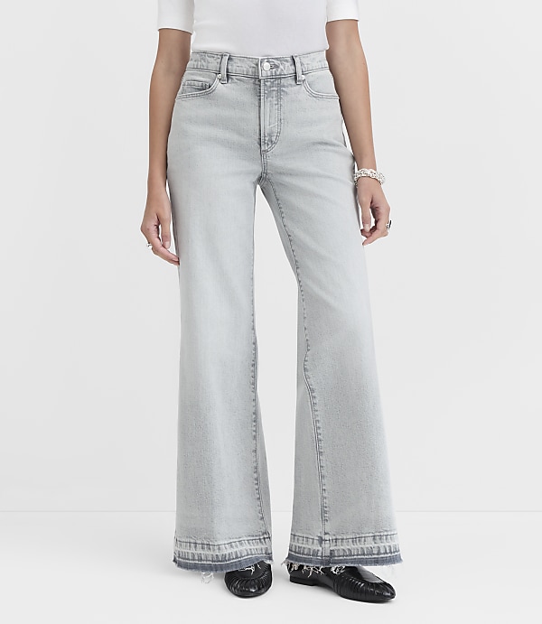 A person stands in light-wash flared jeans with a frayed hem and black shoes against a plain white background.