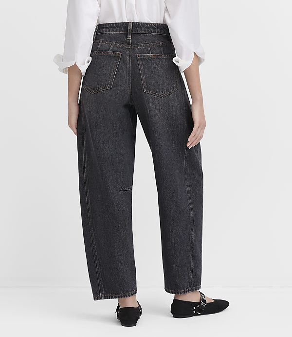 A person wearing dark wash, wide-leg jeans and a white blouse stands against a plain white background.