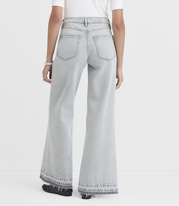 A person wearing light-wash wide-leg jeans with frayed hems stands against a plain white background.