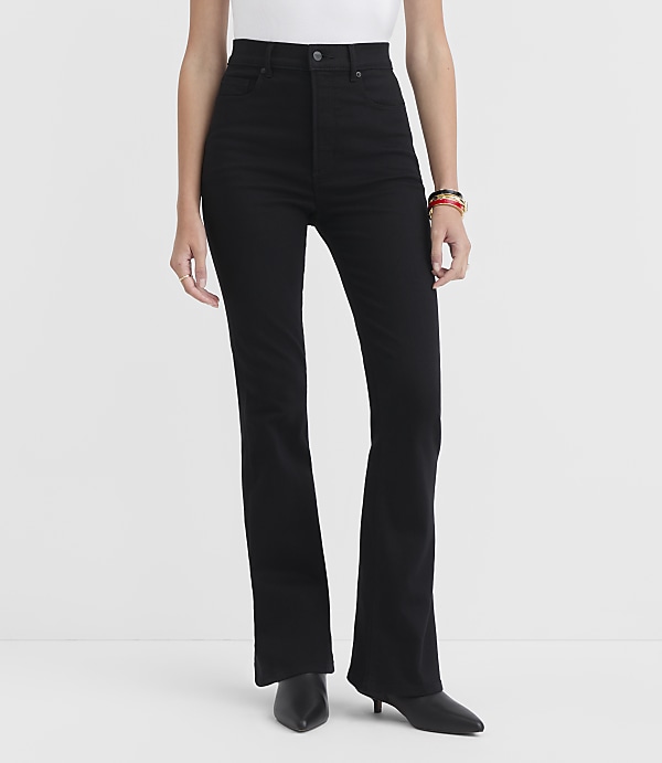 A person wearing black flare jeans and black heeled boots stands against a plain white background.