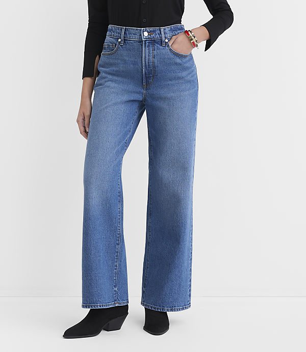 A person wearing wide-leg blue jeans and black boots stands against a plain white background.