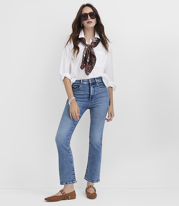A woman in a white shirt, blue jeans, and brown flats stands against a plain white background.