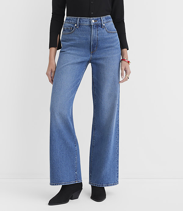 A person wearing high-waisted, wide-leg blue jeans and black boots stands against a plain white background.