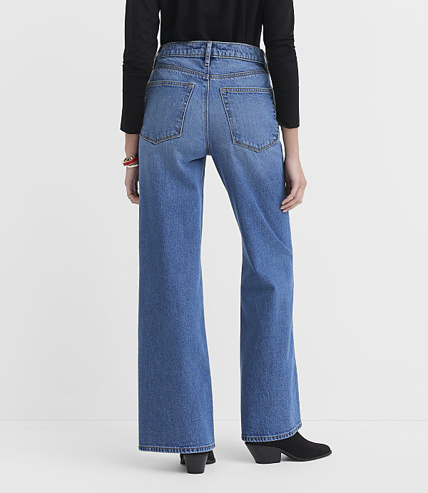 A person wearing wide-leg blue jeans and black boots stands against a plain white background.