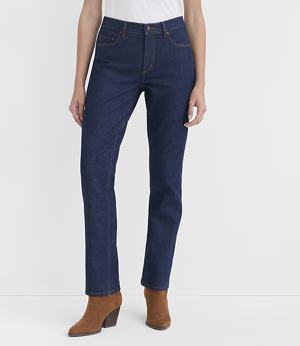 A woman in dark wash jeans and brown ankle boots stands against a plain white background.