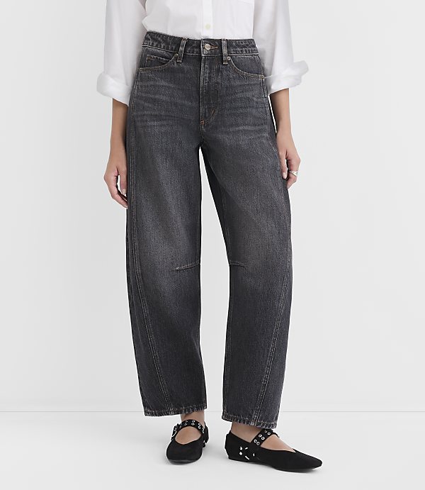 A person stands in the foreground wearing dark wash, wide-leg jeans and black flats, against a plain white background.