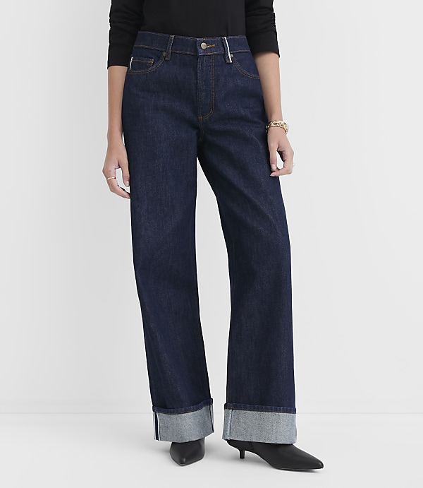 A person stands in dark wash, wide-leg jeans with cuffed hems and black heels against a plain white background.