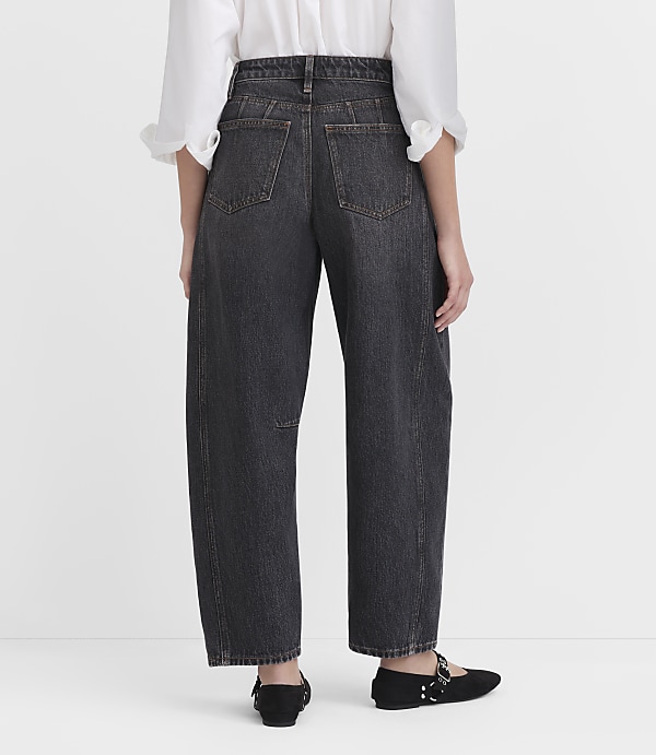 A person wearing dark wash, wide-leg jeans and black flats stands against a plain white background.