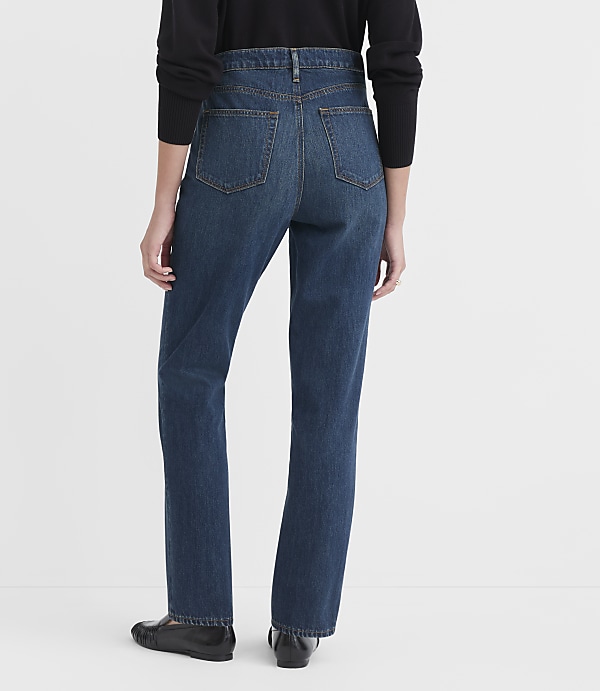 A person wearing dark blue jeans and black shoes stands against a plain white background.