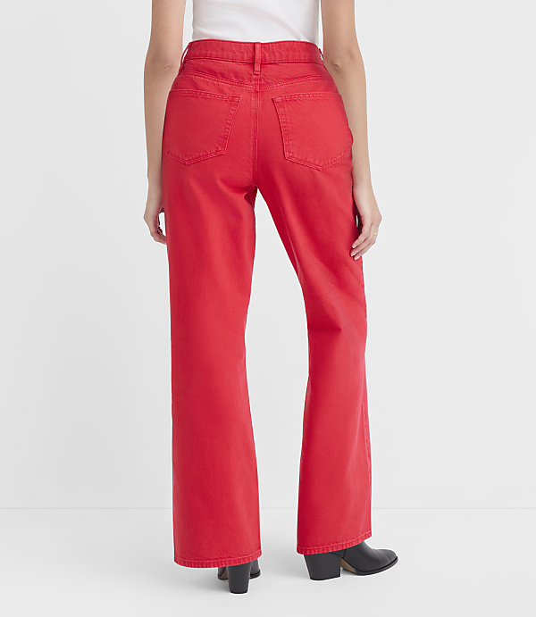 A person wearing bright red wide-leg jeans and black boots stands against a plain white background.