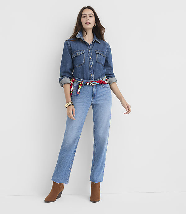 A woman in a denim shirt and jeans stands against a plain white background.