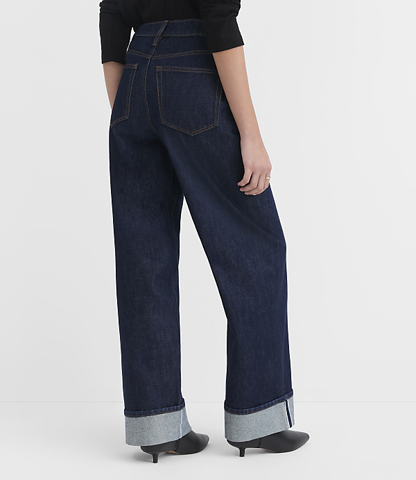 A person wearing dark wash, wide-leg jeans with cuffed hems stands against a plain white background.