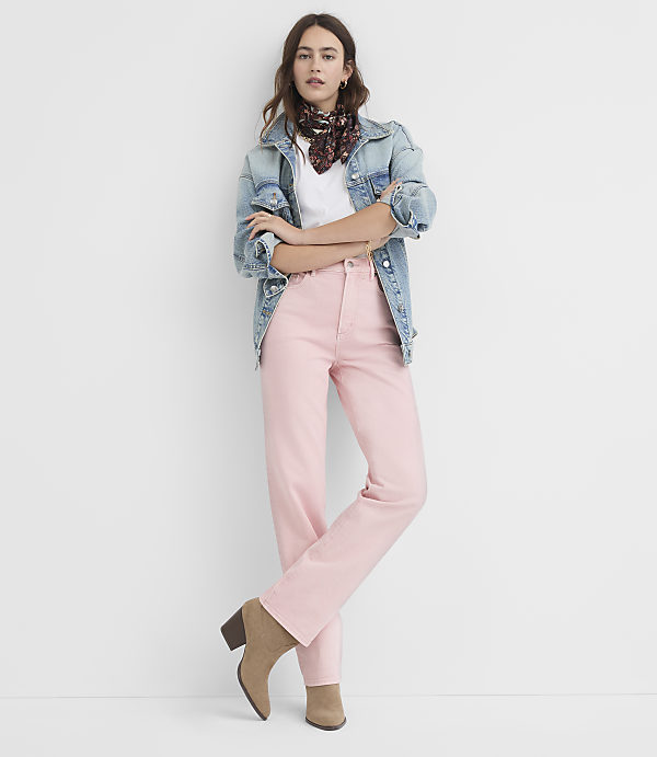 A woman in a denim jacket and pink pants stands against a plain white background.