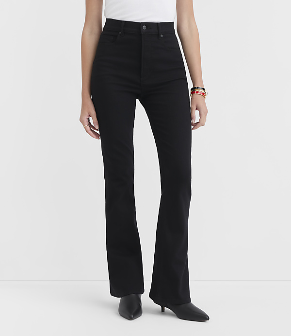 A person stands in black flare jeans and black heels against a plain white background.