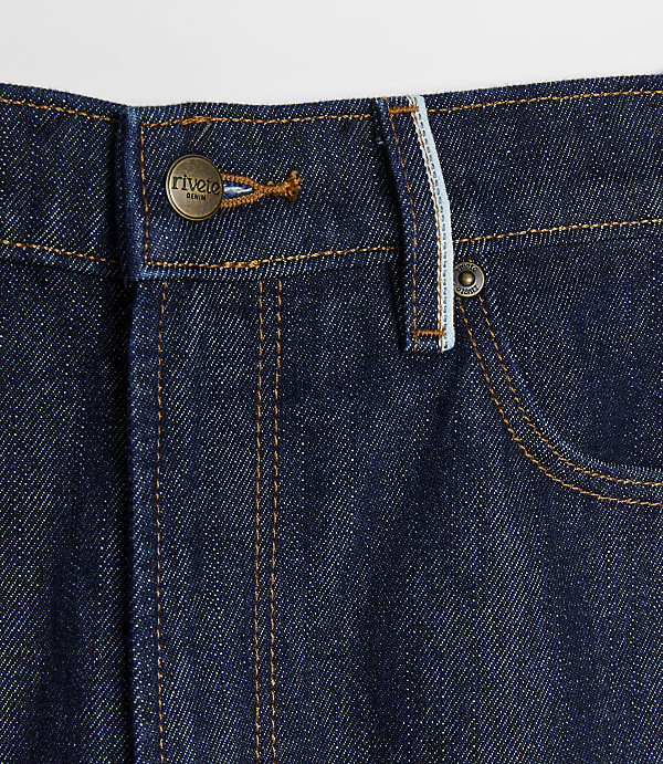 Dark wash denim jeans with copper button and stitching in the foreground are set against a plain white background.