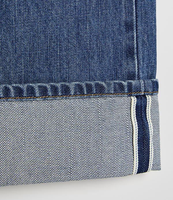 A close-up of cuffed blue denim jeans with a white background.