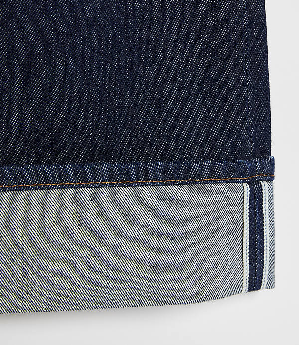 A close-up of dark indigo denim jeans with a cuffed hem showing the lighter interior fabric and selvedge edge against a plain white background.