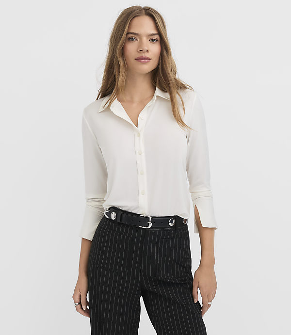 A woman in a white blouse and pinstripe pants stands against a plain white background.