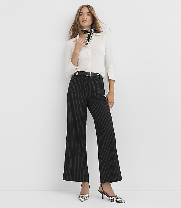 A woman in a white blouse, black pinstripe pants, and patterned heels stands against a plain white background.