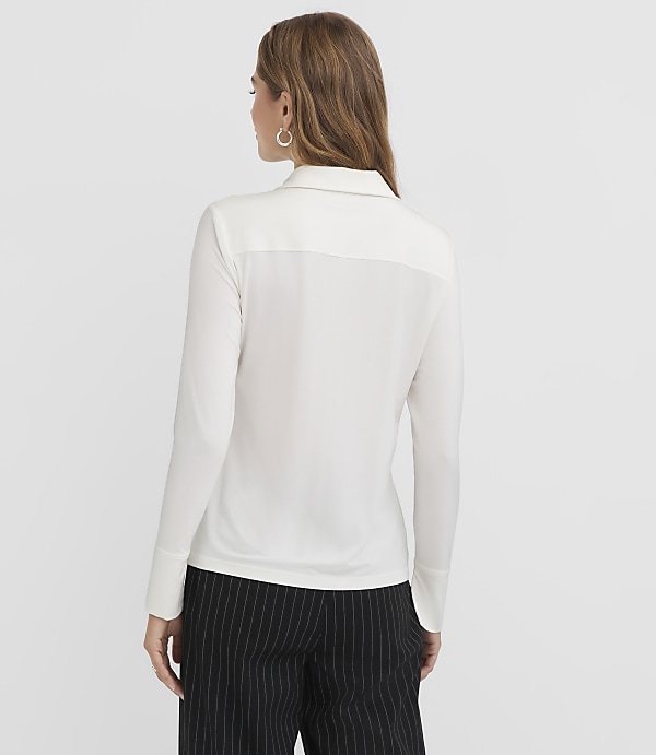 A woman in a white collared shirt and pinstripe pants stands against a plain white background.