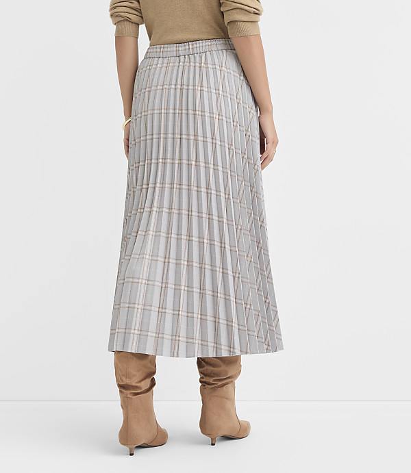 A person wearing a plaid pleated skirt and brown boots stands against a plain white background.
