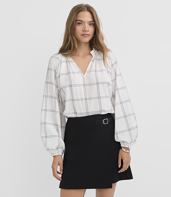 A woman in a white plaid blouse and black skirt stands against a plain white background.