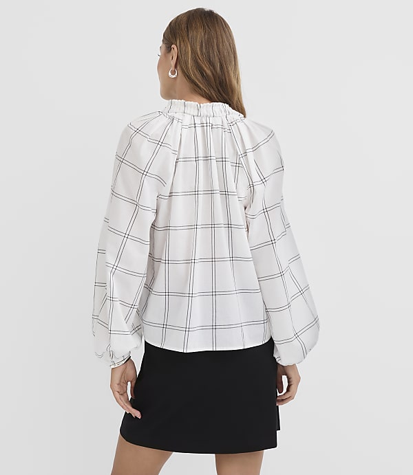 A woman in a white plaid blouse and black skirt stands against a plain white background.