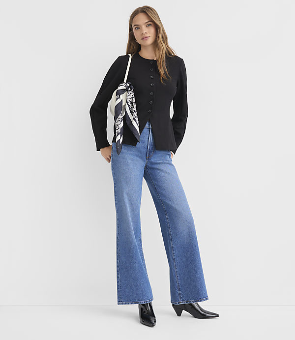 A woman in a black top and wide-leg jeans stands against a plain white background.