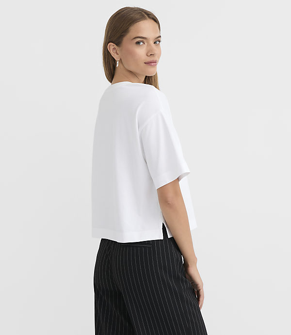 A woman in a white t-shirt and pinstripe pants stands against a plain white background.