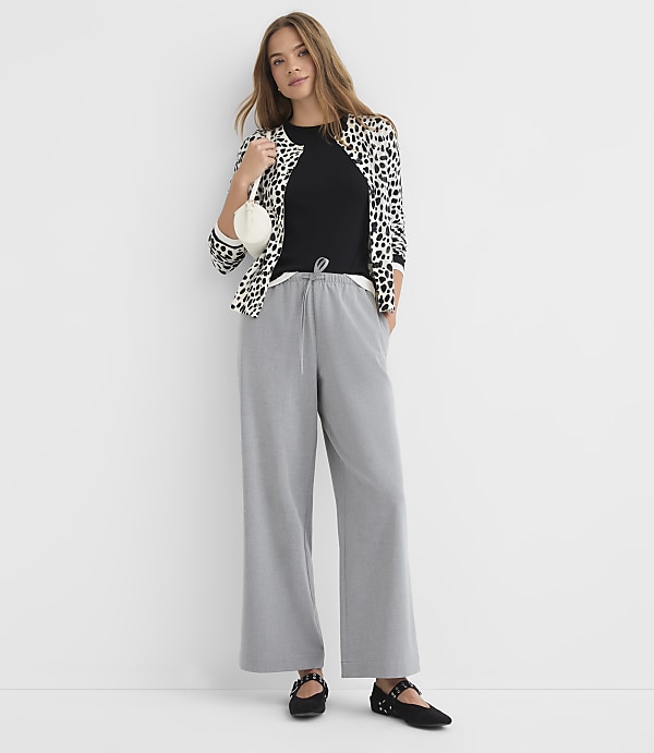 A woman in a leopard print jacket and gray pants stands against a plain white background.