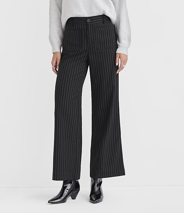 A person stands in black pinstripe wide-leg pants and shiny black boots against a plain white background.