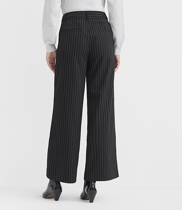 A person wearing black pinstripe wide-leg pants and black heeled boots stands against a plain white background.