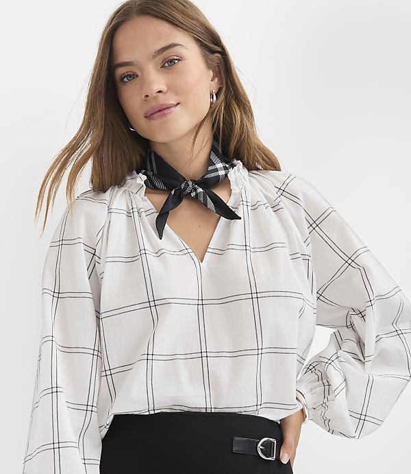 A woman in a white checkered blouse and black scarf poses against a plain white background.