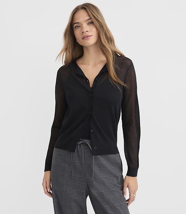 A woman in a black cardigan and plaid pants stands against a plain white background.