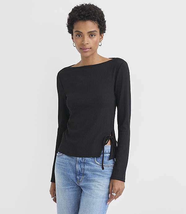 A woman in a black ribbed top and blue jeans stands against a plain white background.