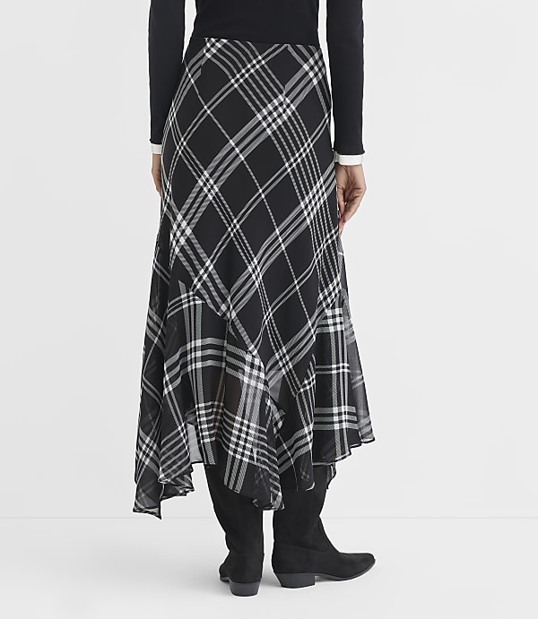 A person wearing a black and white plaid skirt and black boots stands against a plain white background.