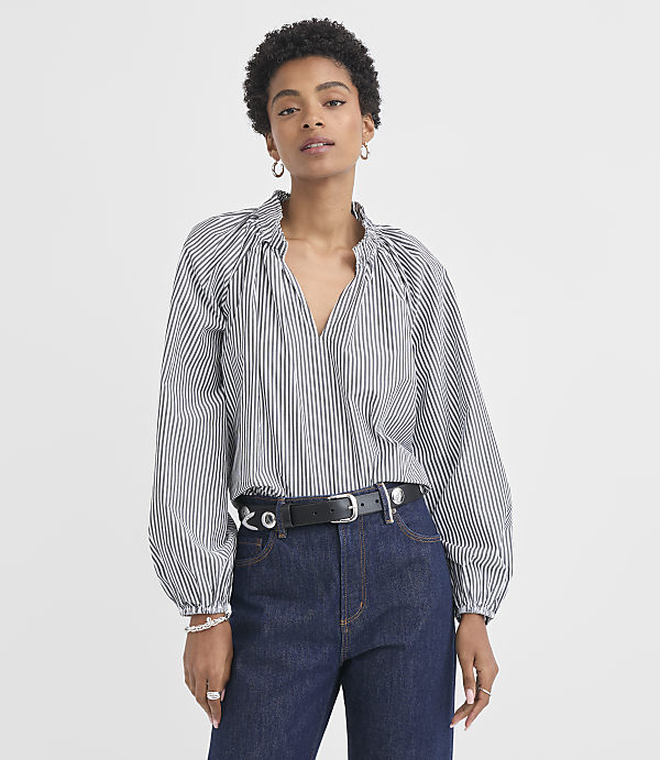 A woman in a striped blouse and jeans stands against a plain white background.