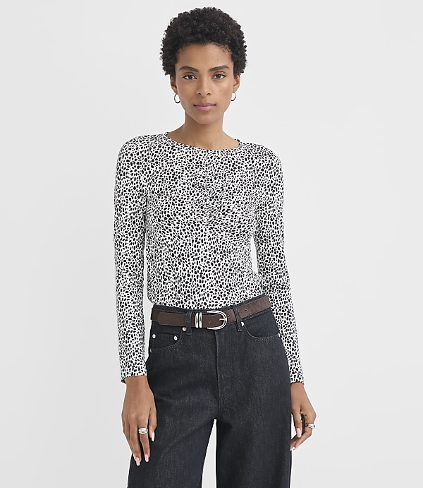 A woman with short dark hair and a leopard-print long-sleeved shirt stands against a plain white background.