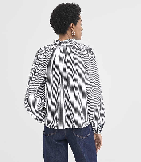 A woman wearing a black and white striped blouse and dark jeans stands against a plain white background.