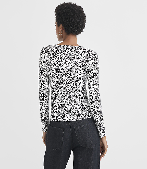 A woman in a dalmatian-print long-sleeved shirt and dark jeans stands against a plain white background.
