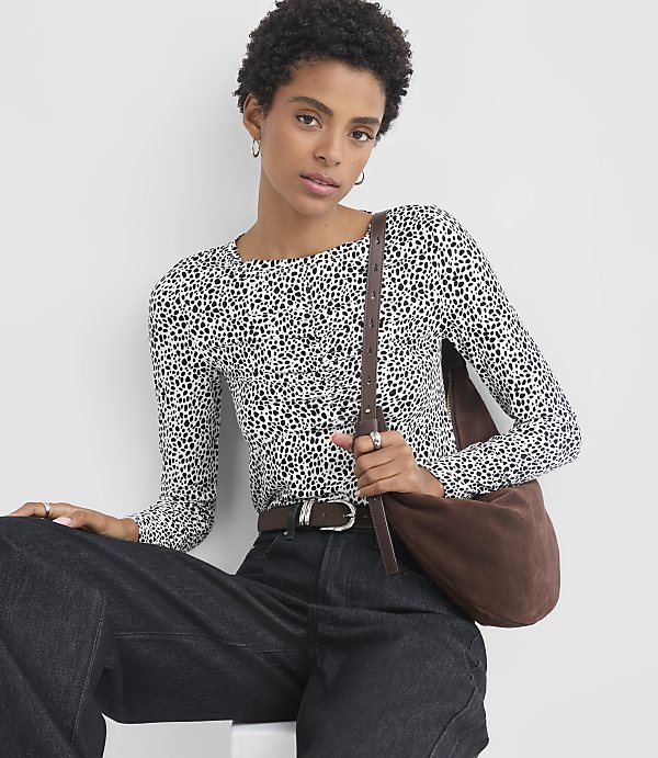 A woman in a dalmatian-print top and dark jeans poses against a plain white background.